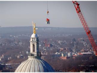 A wide shot of the independent man statue on the statehouse with the crane visible and providence in the background
