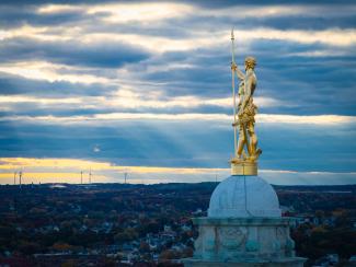 independent man statue on top of the statehouse on a cloudy day with the sun breaking through the clouds